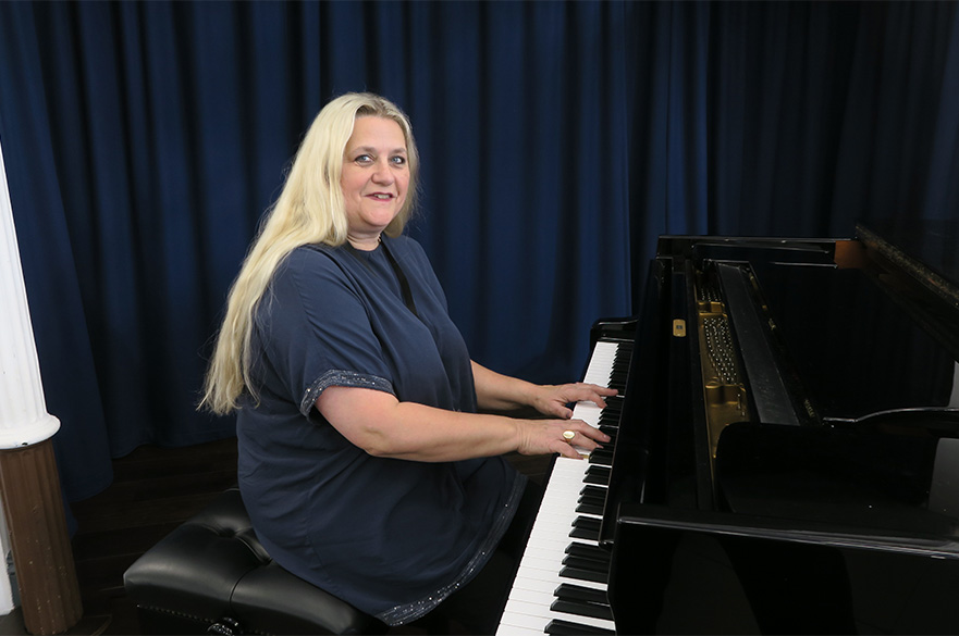 A woman sat at a piano looking at the camera