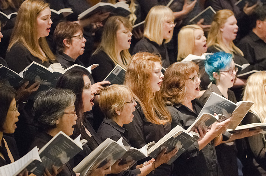 Women singing in a choir, holding music booklets.