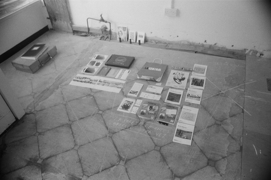 A black and white image of papers and artefacts laid out on the floor.