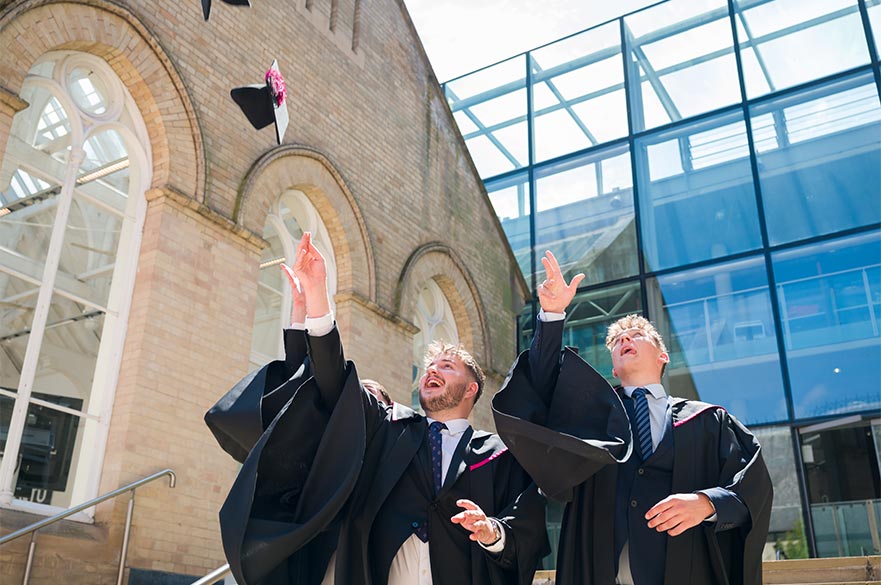 Two graduating students throwing their caps into the sky