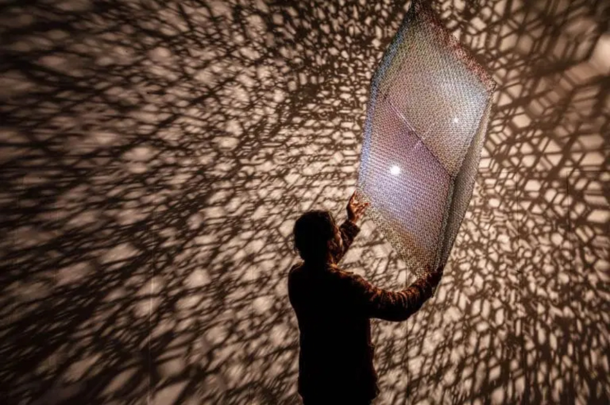 A person holding up a panel which the light hits and refracts a pattern all around the rooms.