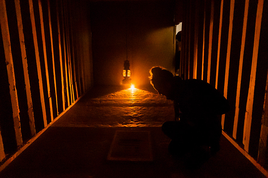 A woman in a dimly lit corrugated cardboard shipping containers at the Knees Kiss Ground exhibition.