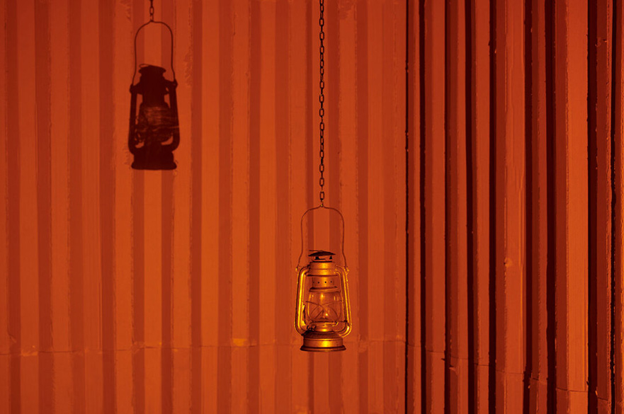 An old fashion lamp hanging with a shadow on a red curtain behind it.